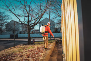 Technician applying perimeter pest control treatment around home foundation in Chantilly, Virginia